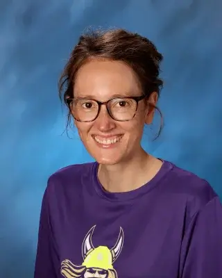 A teacher smiling in front of a blue background.