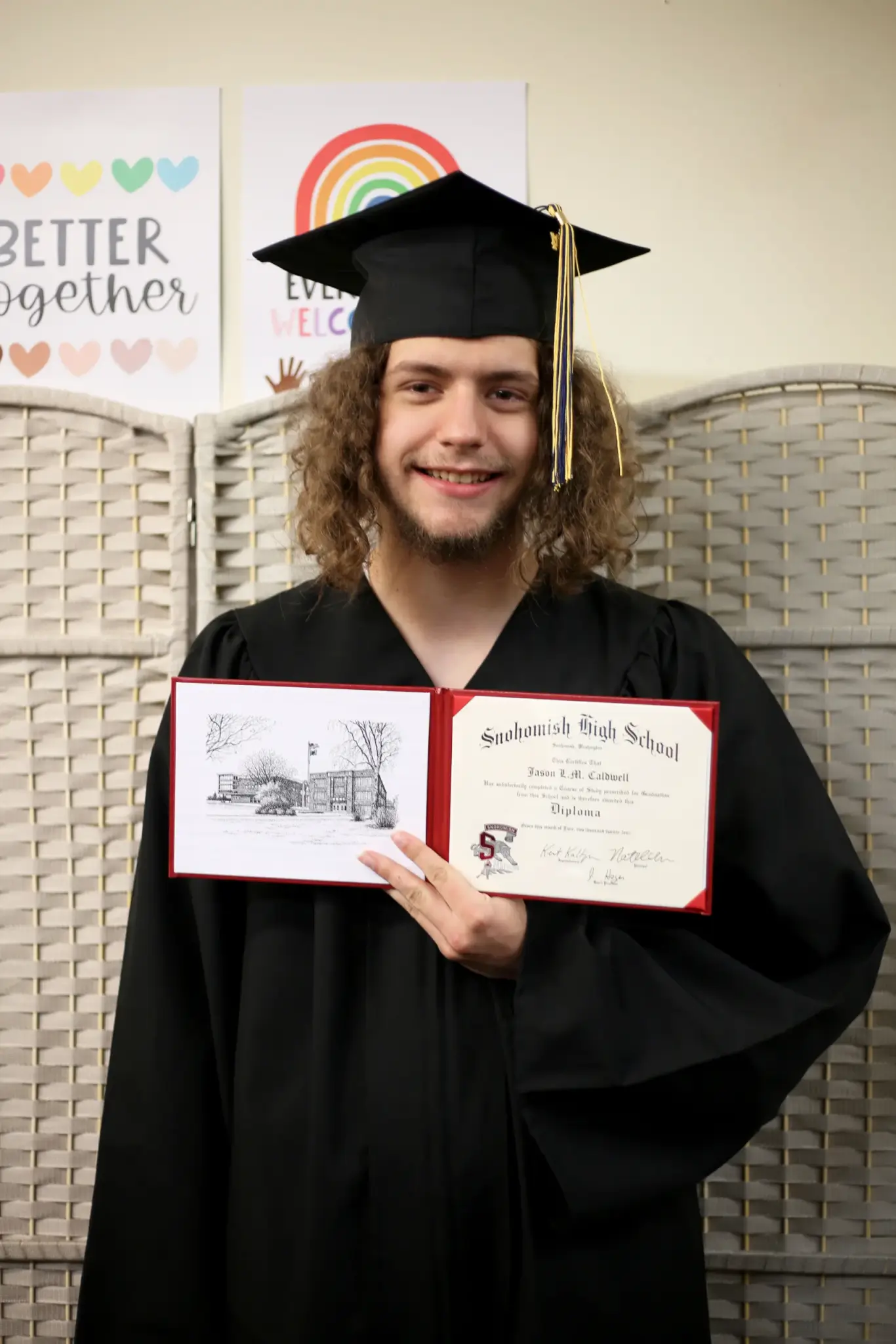 A man in a graduation robe and hat smiles and holds up a diploma.