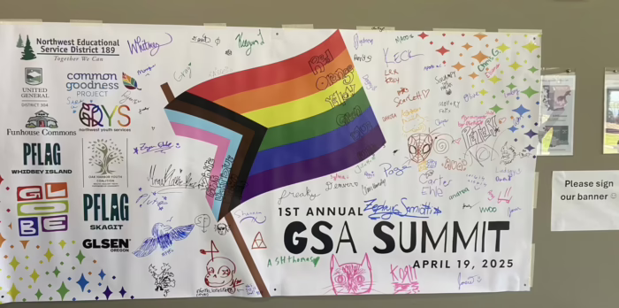 A banner with a rainbow flag and sponsors, signed by attendees of the summit